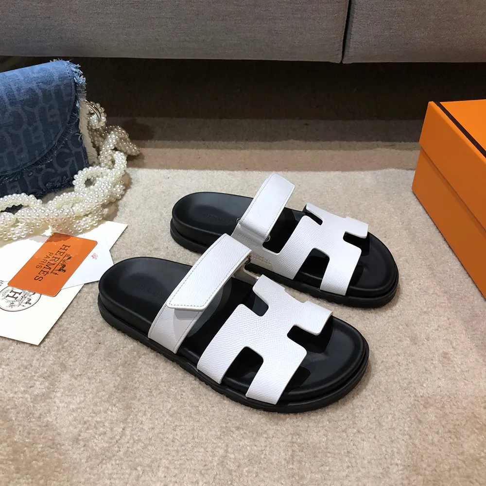 Close-up detail of white leather and Hermes signature 'H' on sandal