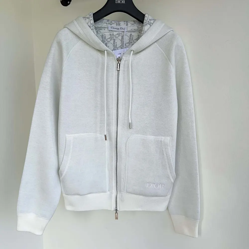 Close-up of signature Dior hardware on white hooded track jacket
