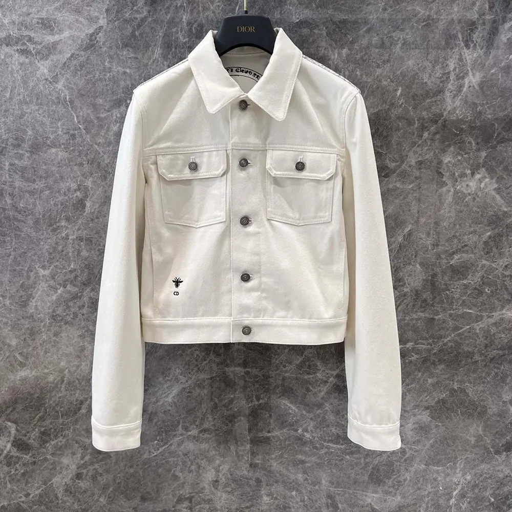 Close-up of gold-tone Dior Around the World motif on white denim jacket
