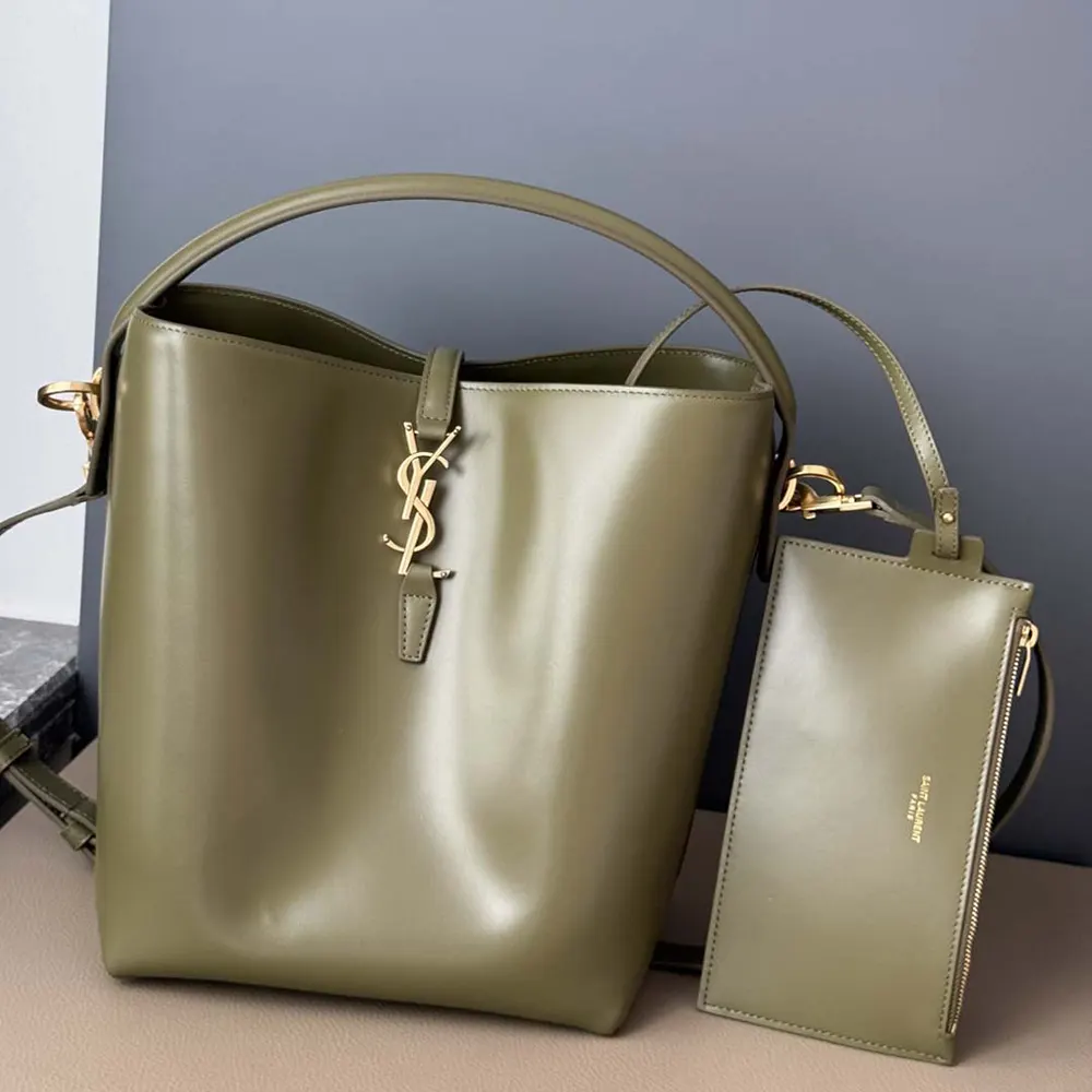 Close-up of gold YSL logo hardware on dark green shiny leather bag