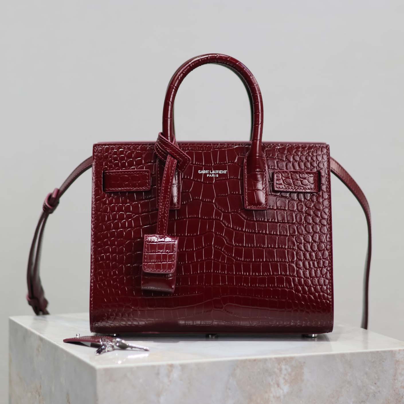 Close-up of gold YSL logo on maroon crocodile embossed leather bag