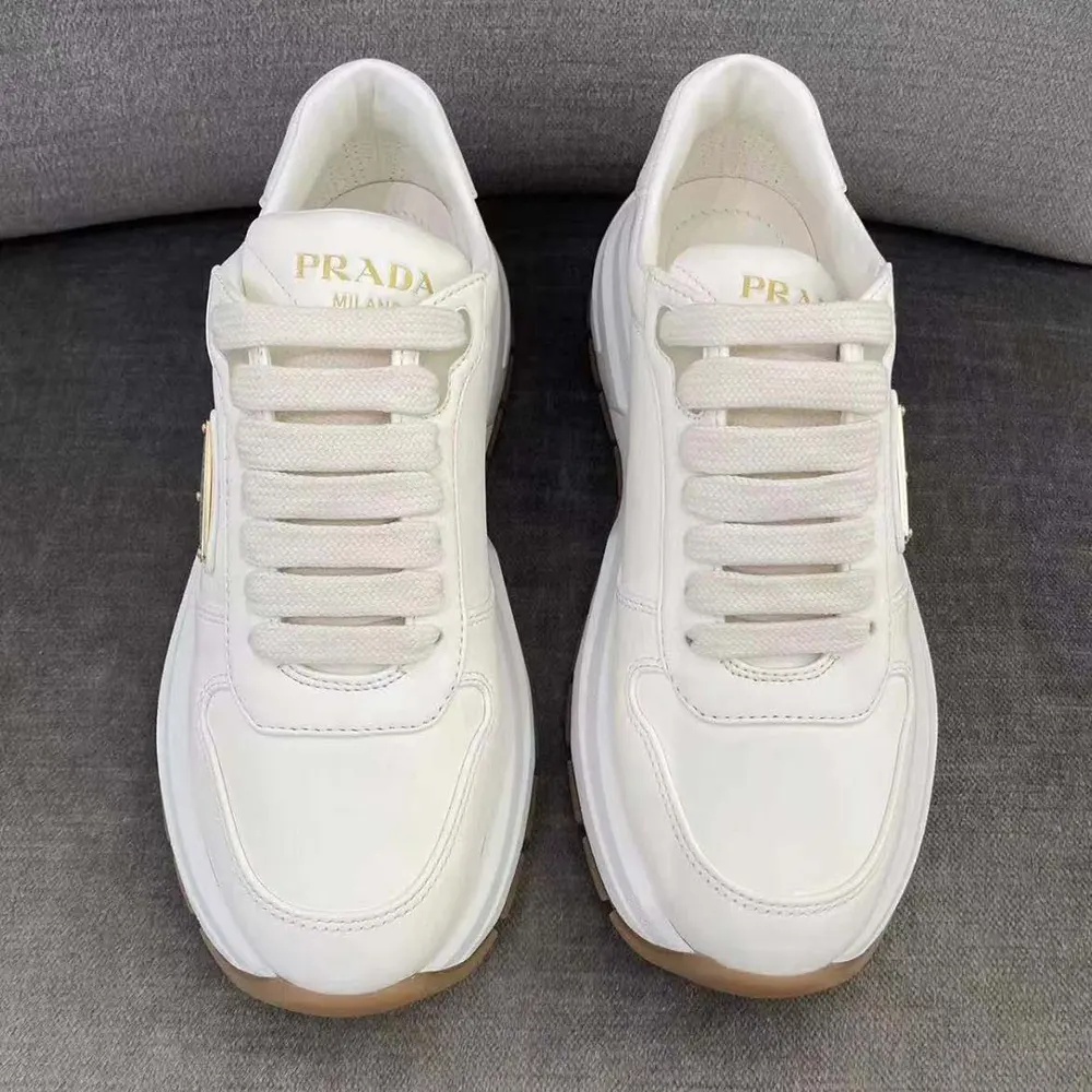 Close-up of Prada triangle logo plaque on white leather sneakers