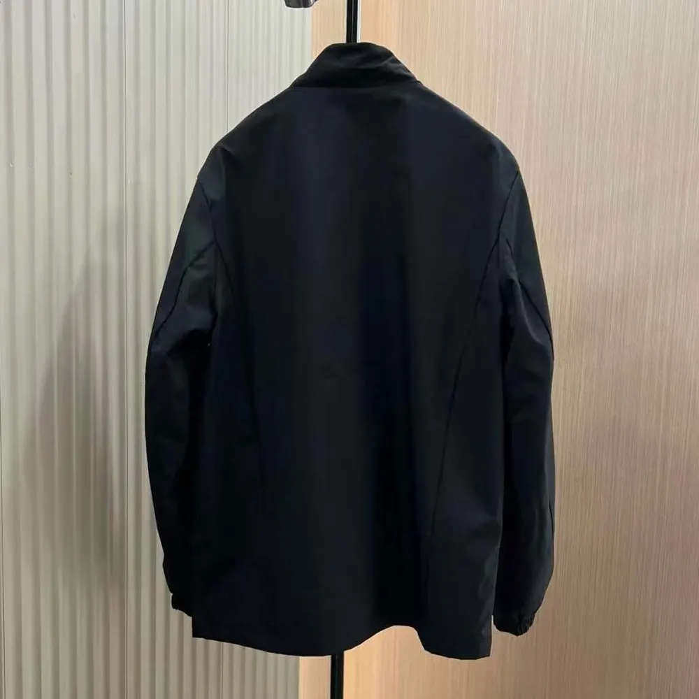 Close-up of Prada triangle metal logo on black Re-Nylon blouson jacket
