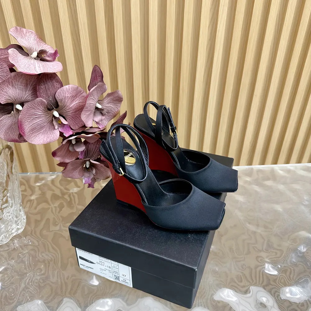 Close-up of gold YSL logo hardware on black satin wedge sandal