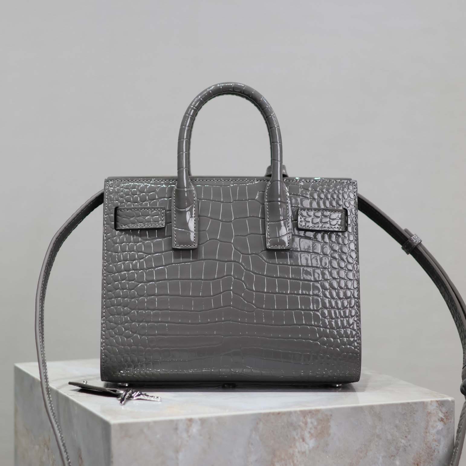 Close-up detail of silver YSL hardware on crocodile embossed leather bag