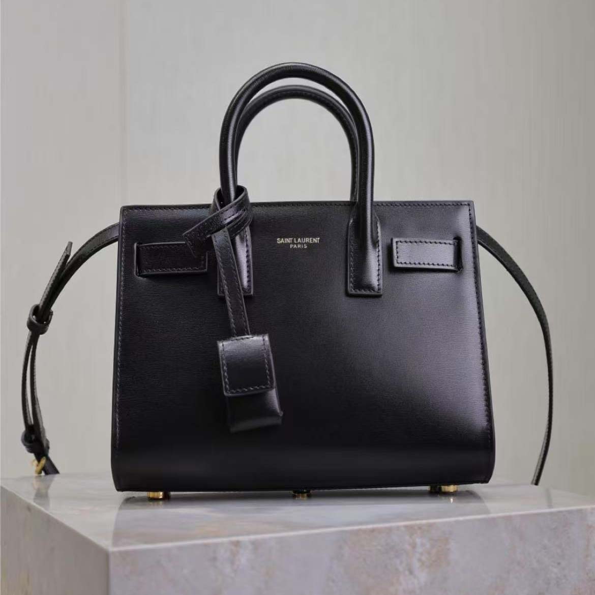 Close-up of gold-tone YSL logo hardware on smooth black leather bag