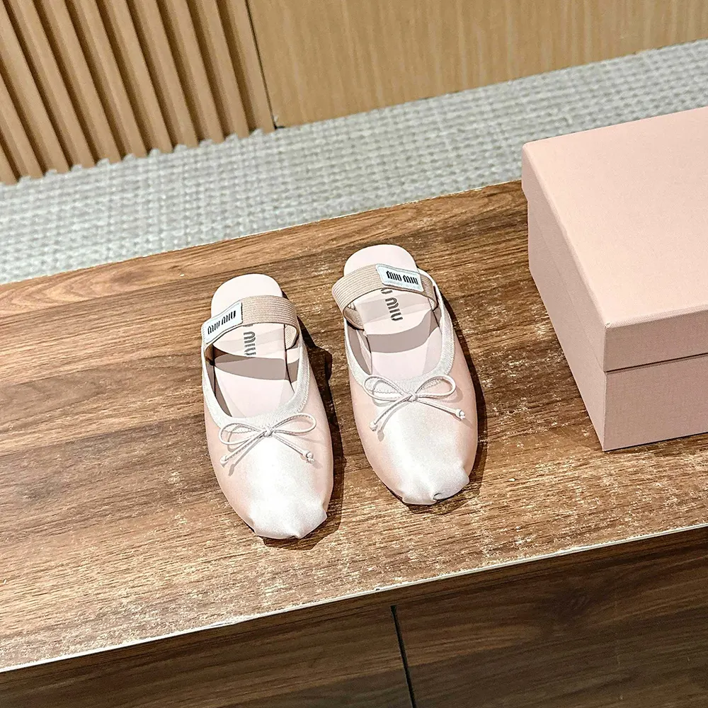 Close-up of pink satin material and metal logo on Miu Miu ballerina mules