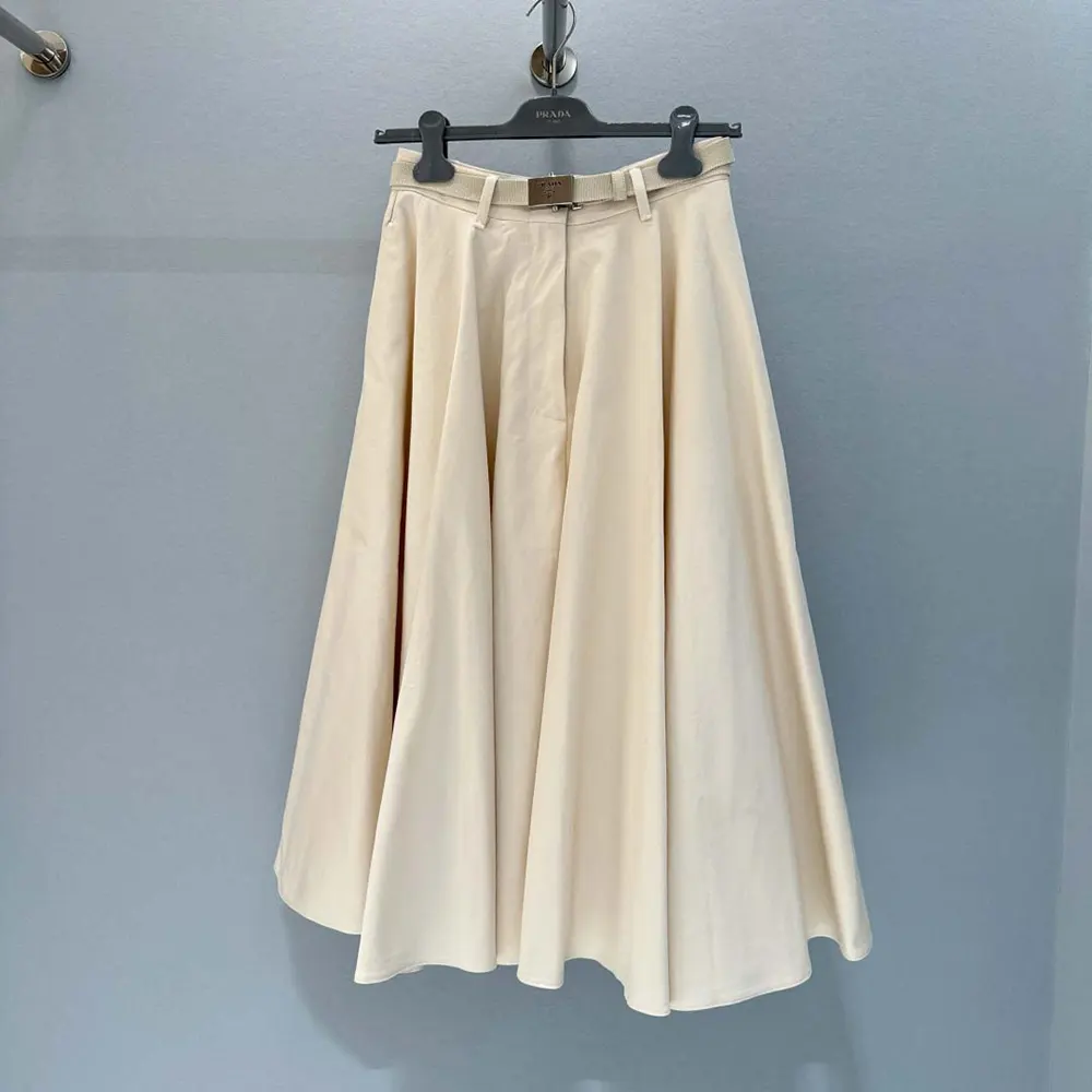 Close-up of Prada metal logo detail on white midi skirt