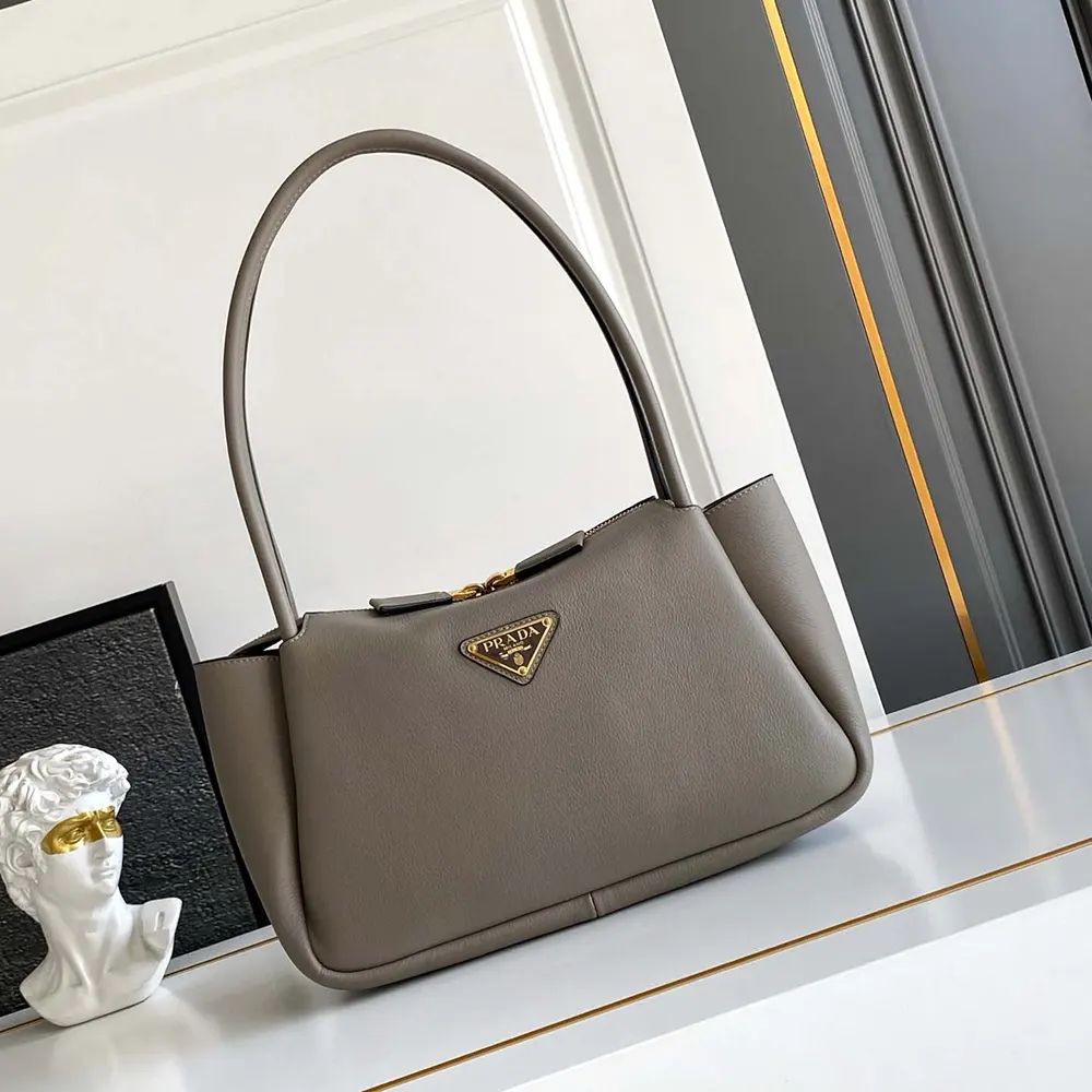 Close-up of silver Prada triangular logo on gray leather shoulder bag