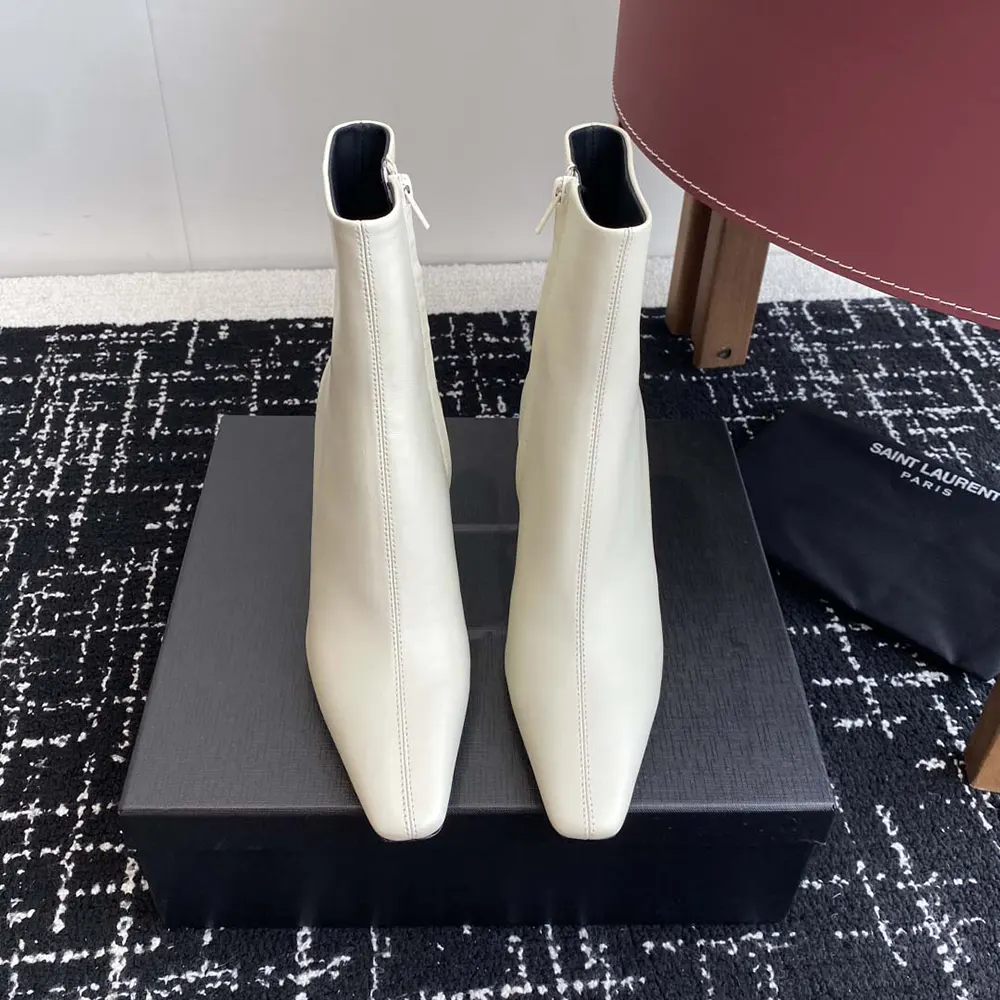 Close-up on gold YSL logo hardware on white leather booties