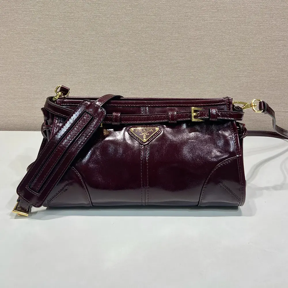 Close-up of gold-tone Prada logo on maroon leather bag