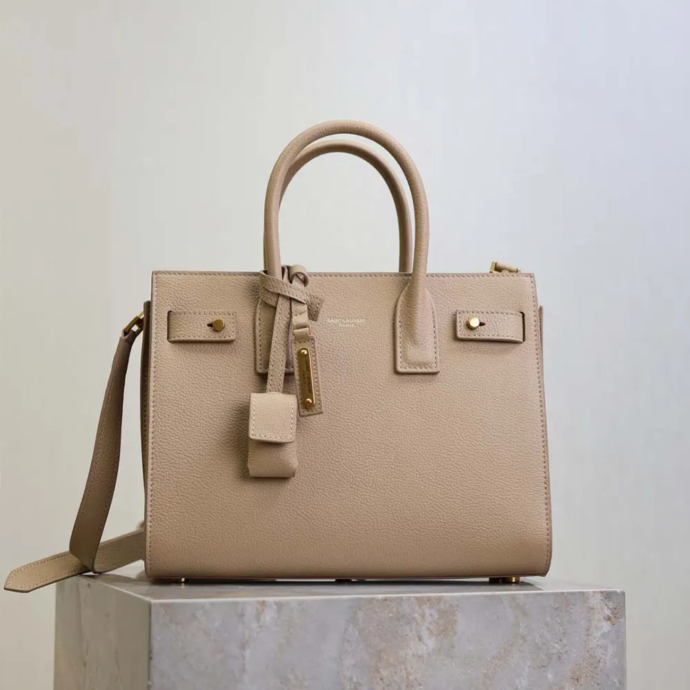Close-up of gold YSL logo hardware on beige Baby Sac De Jour bag