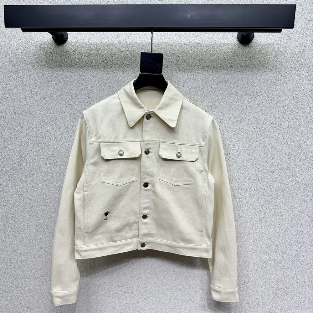 Close-up on gold-tone Dioresque Stella motif on white cotton denim jacket