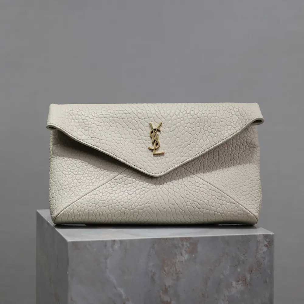 Close-up of iconic YSL gold-tone logo on white envelope pouch