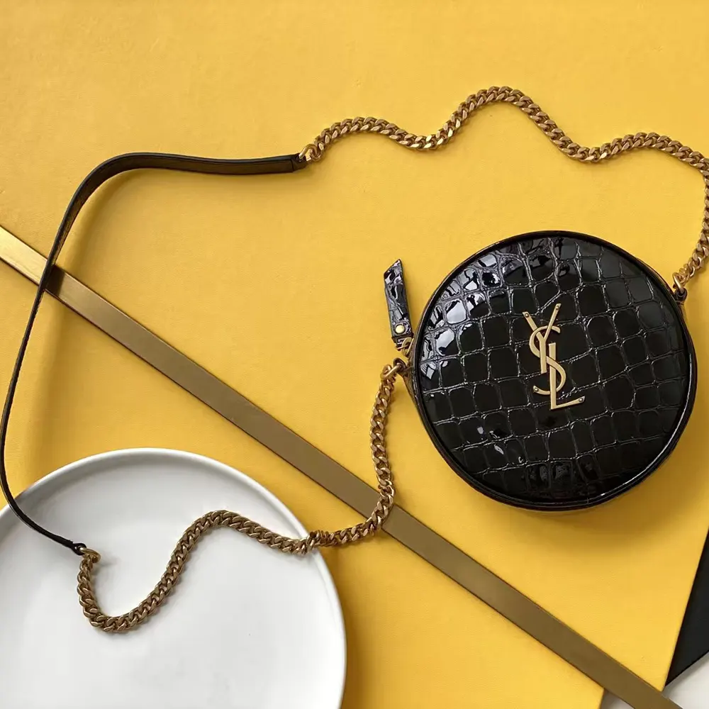 Close-up on antique gold YSL logo hardware on black patent leather bag
