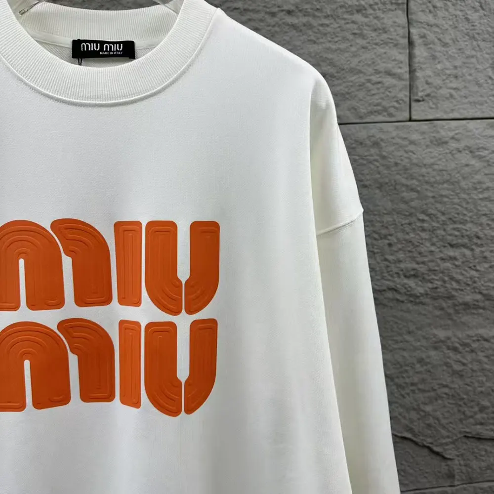 Close-up of orange cotton fabric and logo embroidery detail on sweatshirt