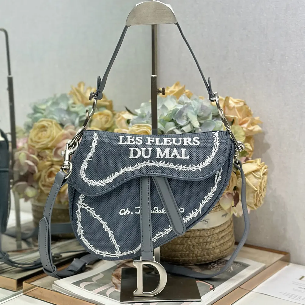 Close-up detail of blue leather and white book cover embroidery on Dior saddle bag