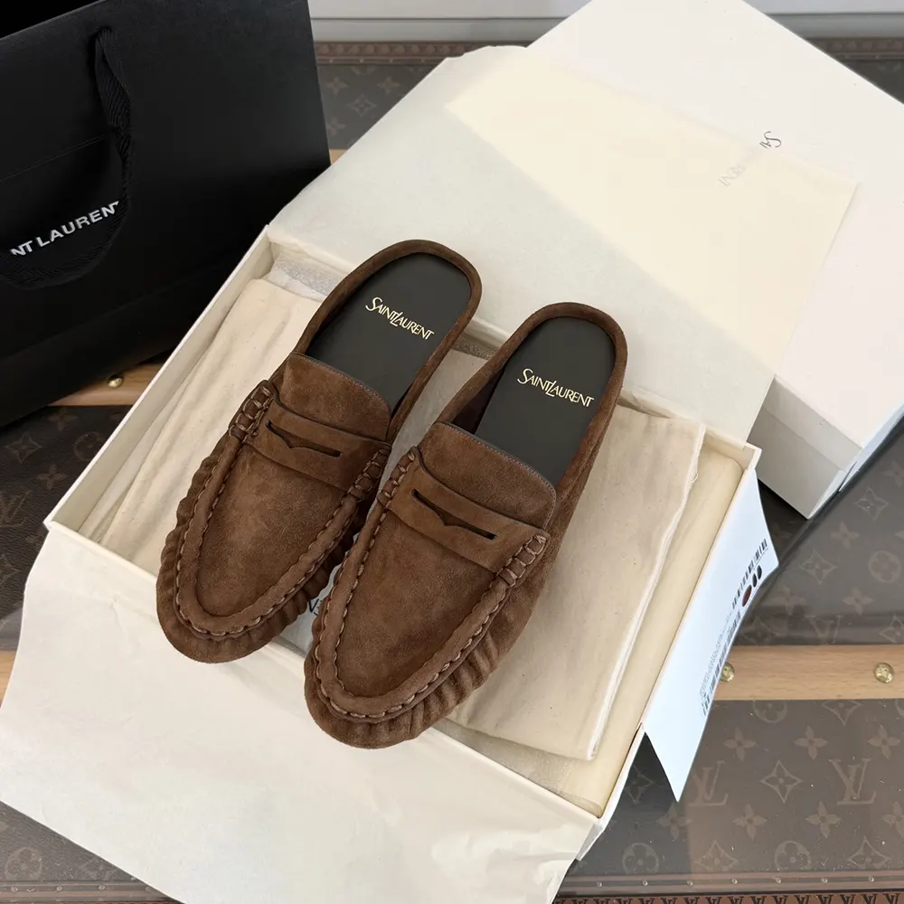 Close-up of gold YSL logo hardware on brown suede loafers