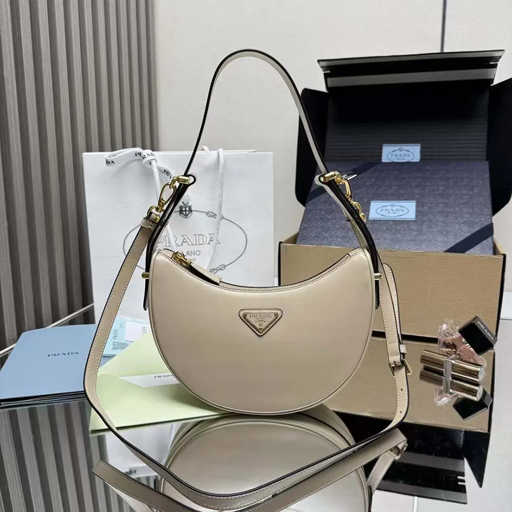 Close-up of gold-tone Prada logo on sandy leather bag