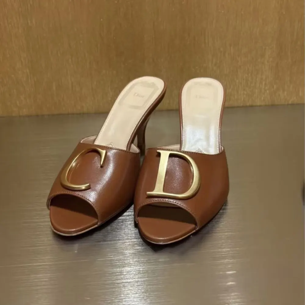 Close-up of gold Dior initials hardware on brown lambskin slide