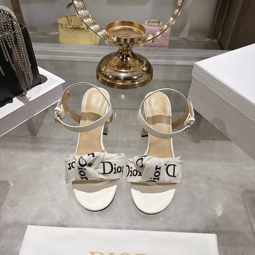 Close-up of white embroidery and gold J’Adior hardware on sandal