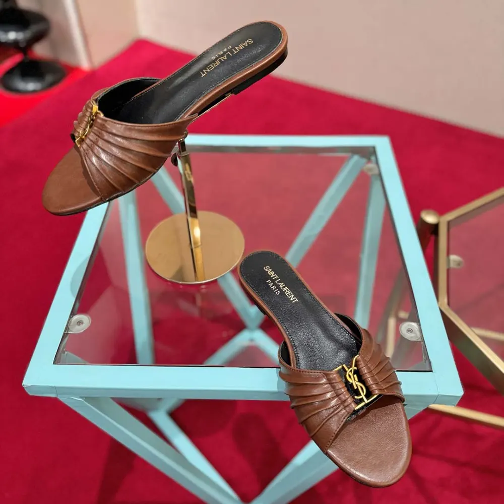 Close-up of gold YSL logo on brown smooth leather slides