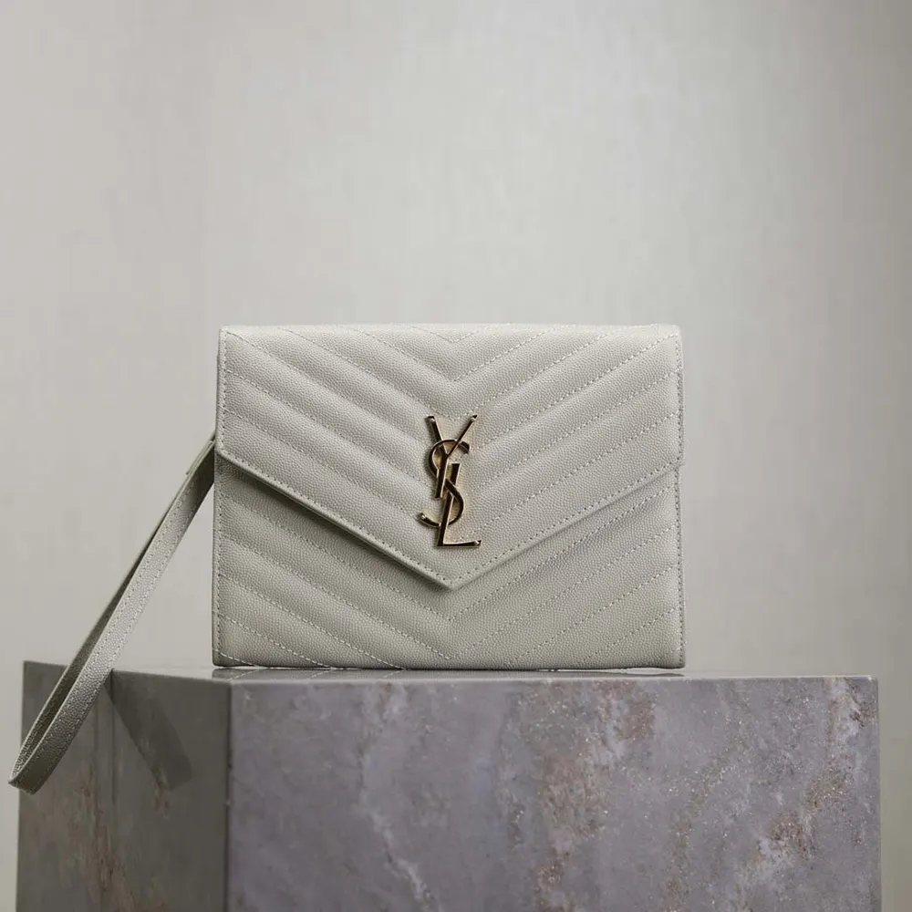 Close-up of gold YSL logo and flap closure on white Cassandre pouch