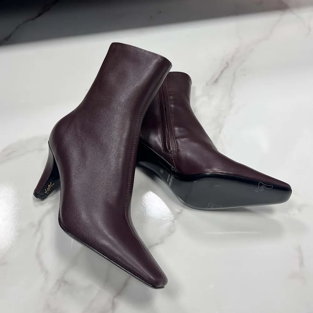 Close-up on gold YSL logo hardware on smooth leather booties